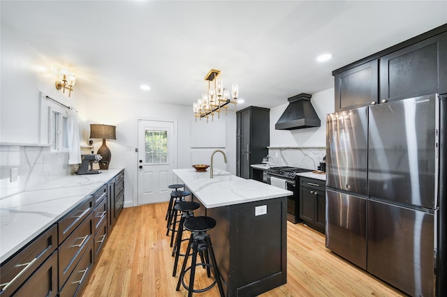 kitchen with range with gas cooktop, custom exhaust hood, decorative backsplash, stainless steel refrigerator, and a kitchen island with sink