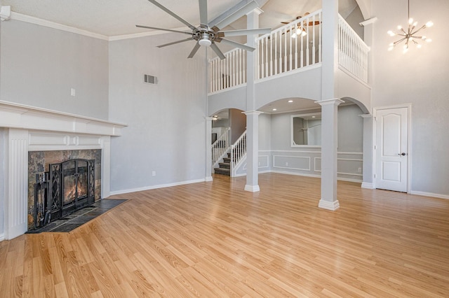 unfurnished living room featuring a tile fireplace, a high ceiling, light hardwood / wood-style flooring, ornamental molding, and ceiling fan with notable chandelier