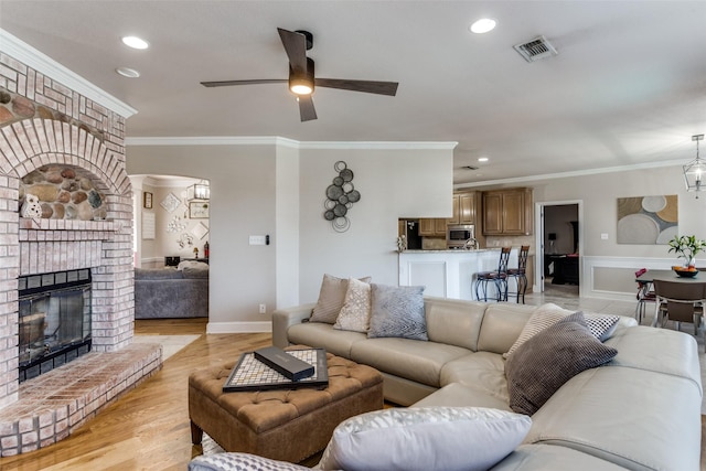 living room featuring a brick fireplace, light hardwood / wood-style flooring, crown molding, and ceiling fan