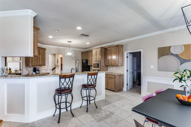 kitchen with crown molding, appliances with stainless steel finishes, decorative light fixtures, kitchen peninsula, and light stone counters