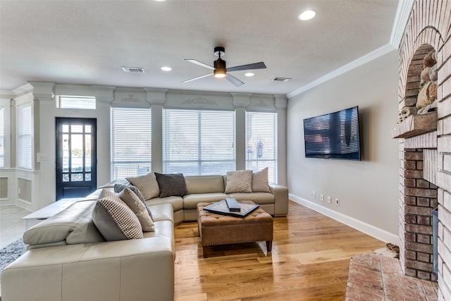 living room featuring light hardwood / wood-style flooring, ceiling fan, a fireplace, a textured ceiling, and ornamental molding