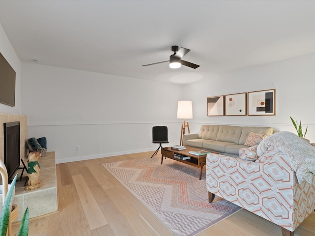 living room featuring a tiled fireplace, light hardwood / wood-style flooring, and ceiling fan