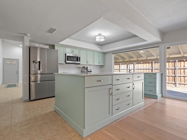 kitchen with sink, green cabinetry, appliances with stainless steel finishes, a tray ceiling, and decorative backsplash