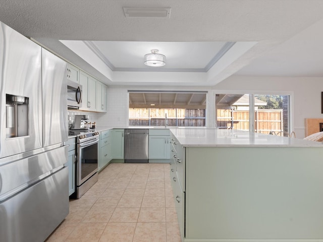 kitchen with light tile patterned flooring, tasteful backsplash, green cabinetry, appliances with stainless steel finishes, and a raised ceiling