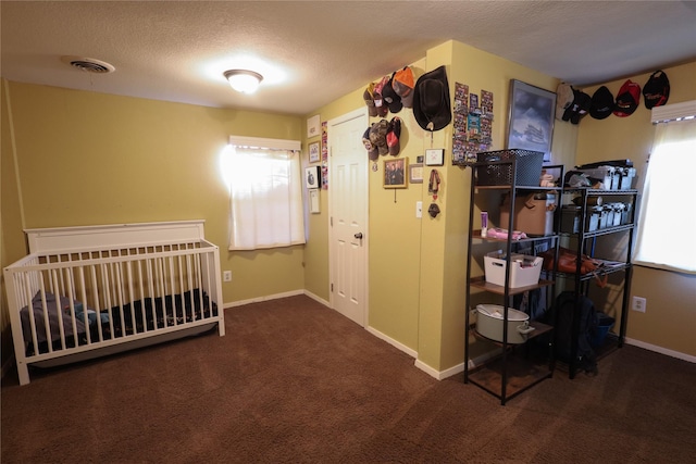 bedroom featuring a textured ceiling, dark colored carpet, and a nursery area