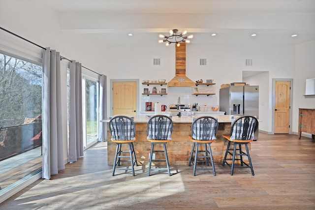 kitchen featuring stainless steel refrigerator with ice dispenser, decorative backsplash, a kitchen bar, light wood-type flooring, and a chandelier