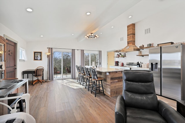 kitchen featuring a kitchen bar, stainless steel appliances, a chandelier, beam ceiling, and light hardwood / wood-style flooring