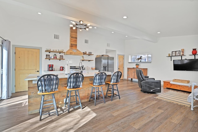 kitchen with stainless steel fridge, tasteful backsplash, a notable chandelier, a kitchen breakfast bar, and beam ceiling