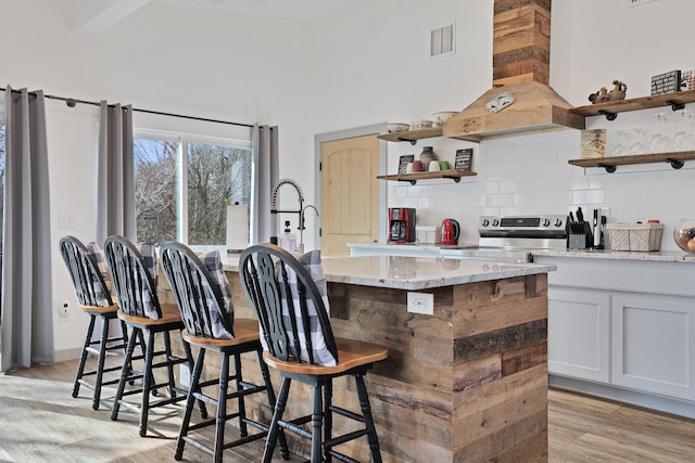 kitchen featuring light stone countertops, custom exhaust hood, a kitchen breakfast bar, a kitchen island with sink, and light wood-type flooring