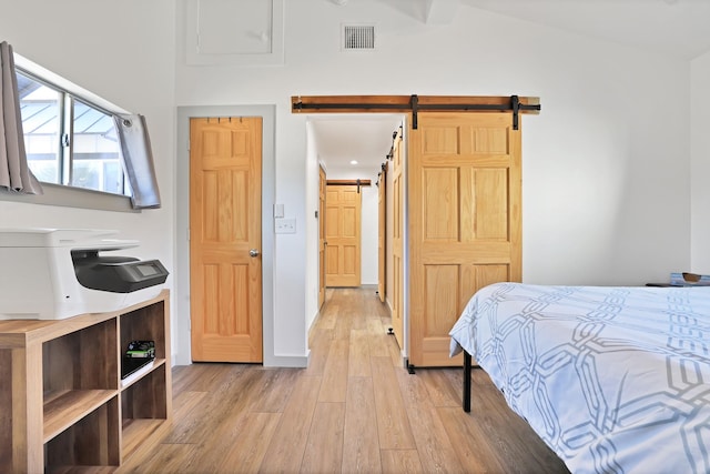 bedroom featuring light wood-type flooring, vaulted ceiling, and a barn door