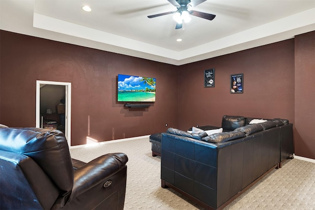 home theater with ceiling fan, light colored carpet, and a tray ceiling