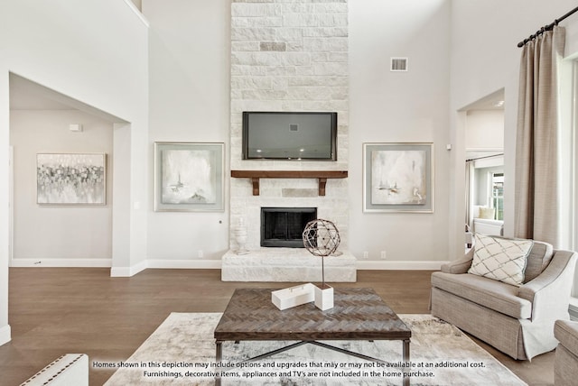 living room with a high ceiling, hardwood / wood-style floors, and a stone fireplace