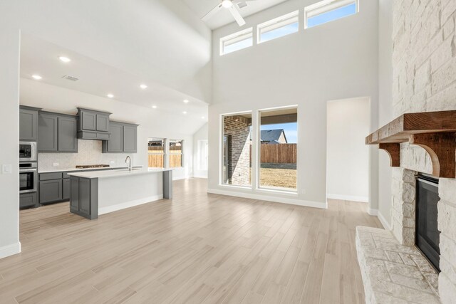 kitchen with appliances with stainless steel finishes, a kitchen island with sink, lofted ceiling, light stone countertops, and pendant lighting