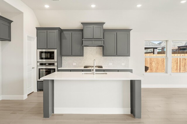 kitchen featuring appliances with stainless steel finishes, dark wood-type flooring, sink, backsplash, and a kitchen island with sink