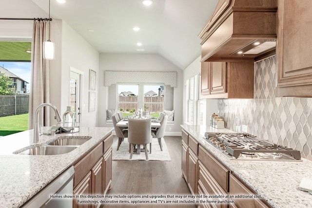 kitchen with pendant lighting, custom exhaust hood, sink, light stone countertops, and appliances with stainless steel finishes