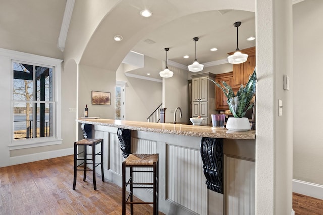 kitchen featuring ornamental molding, light hardwood / wood-style floors, a kitchen bar, and kitchen peninsula