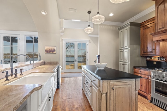 kitchen with white cabinets, stainless steel range, hanging light fixtures, ornamental molding, and light wood-type flooring