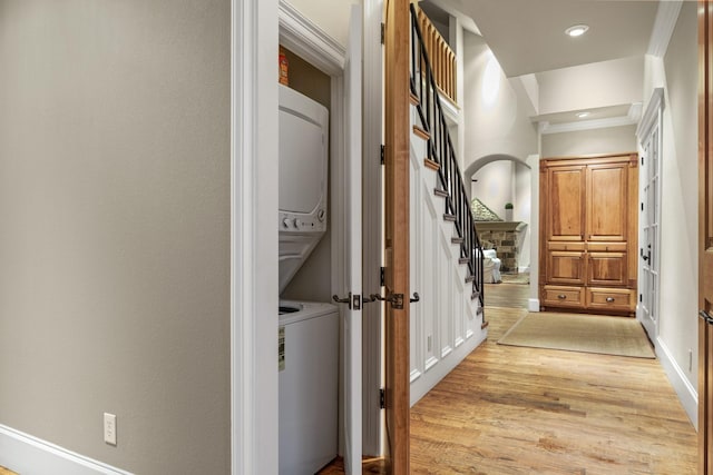 hall with crown molding, stacked washer / drying machine, and light hardwood / wood-style floors