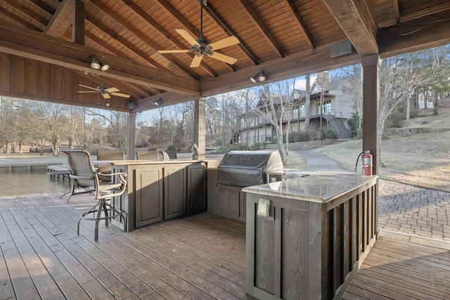 deck with grilling area, ceiling fan, a bar, and exterior kitchen