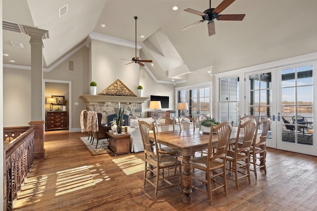 dining space featuring hardwood / wood-style floors, a stone fireplace, ceiling fan, decorative columns, and crown molding