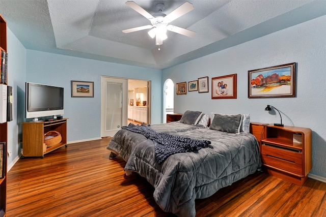 bedroom featuring ceiling fan, ensuite bathroom, dark hardwood / wood-style floors, a raised ceiling, and a textured ceiling