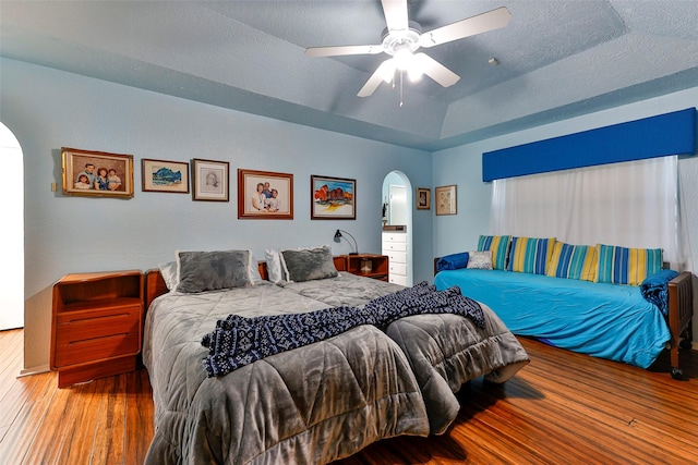 bedroom with ceiling fan, wood-type flooring, a raised ceiling, and a textured ceiling