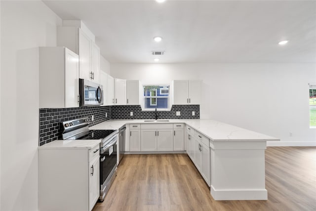 kitchen with kitchen peninsula, appliances with stainless steel finishes, sink, and white cabinetry