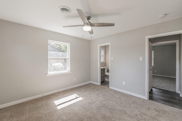 unfurnished bedroom featuring ceiling fan, dark carpet, and ensuite bath