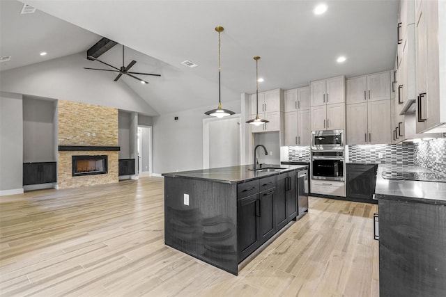 kitchen featuring an island with sink, backsplash, a fireplace, hanging light fixtures, and sink