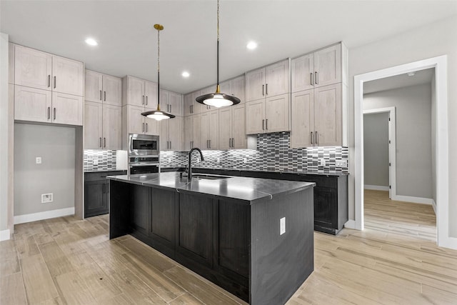 kitchen with appliances with stainless steel finishes, dark countertops, a sink, and light wood-style flooring