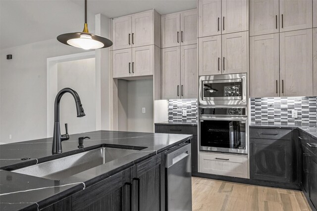 kitchen with a stone fireplace, a kitchen island with sink, dishwasher, hanging light fixtures, and sink