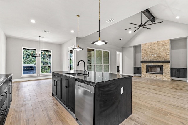 kitchen featuring a stone fireplace, dark cabinets, a sink, visible vents, and stainless steel dishwasher