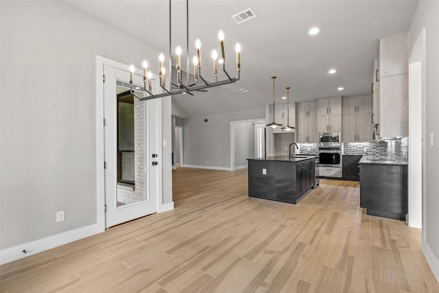 kitchen featuring an inviting chandelier, stainless steel appliances, a kitchen island with sink, hanging light fixtures, and sink