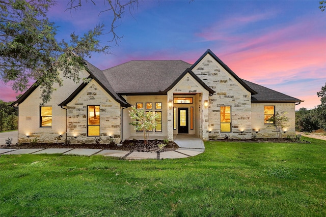 view of front of house with stone siding, brick siding, a front yard, and a shingled roof