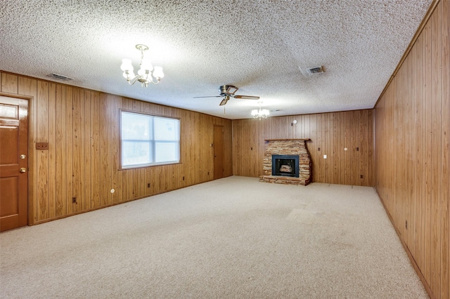 unfurnished living room featuring light carpet, wooden walls, ceiling fan with notable chandelier, and a stone fireplace