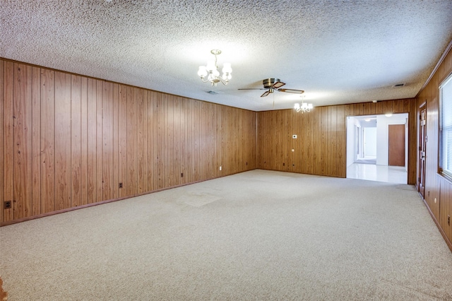 unfurnished room with light carpet, wood walls, ceiling fan with notable chandelier, and a textured ceiling