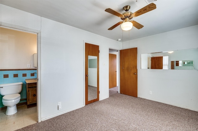 unfurnished bedroom featuring ceiling fan, light colored carpet, tile walls, and ensuite bathroom