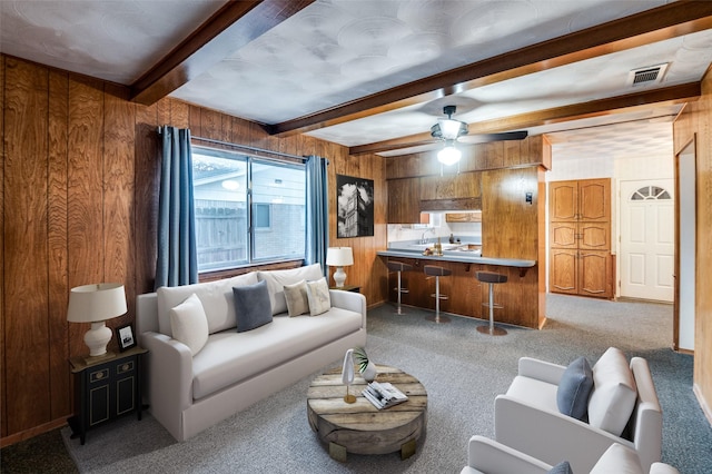 carpeted living room with ceiling fan, wood walls, and beamed ceiling