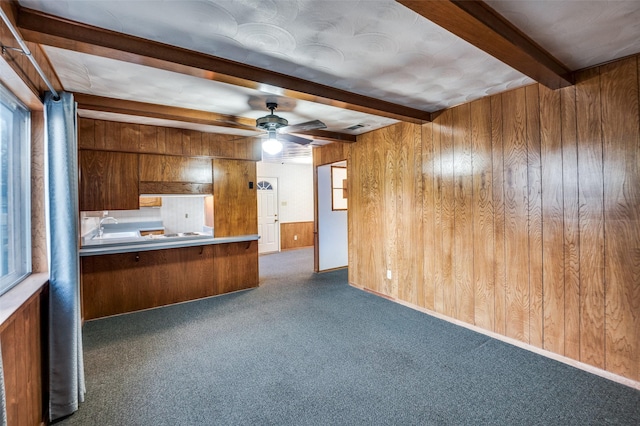 kitchen featuring beam ceiling, ceiling fan, wood walls, and dark carpet