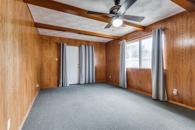 spare room featuring ceiling fan, beam ceiling, carpet floors, and wood walls