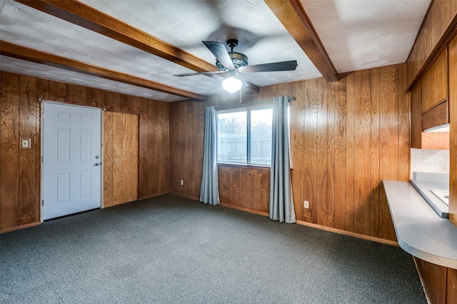 unfurnished room featuring beam ceiling, ceiling fan, wood walls, and dark carpet