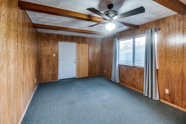 carpeted empty room featuring ceiling fan, beam ceiling, and wood walls