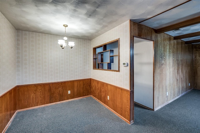 empty room with wooden walls, beam ceiling, a chandelier, and dark colored carpet