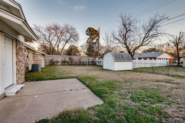 yard at dusk featuring central AC, a storage unit, and a patio