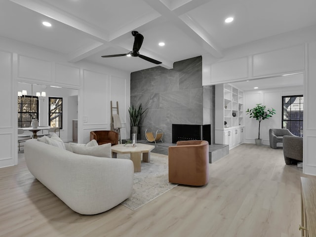 living room with built in shelves, a premium fireplace, beam ceiling, and light wood-type flooring