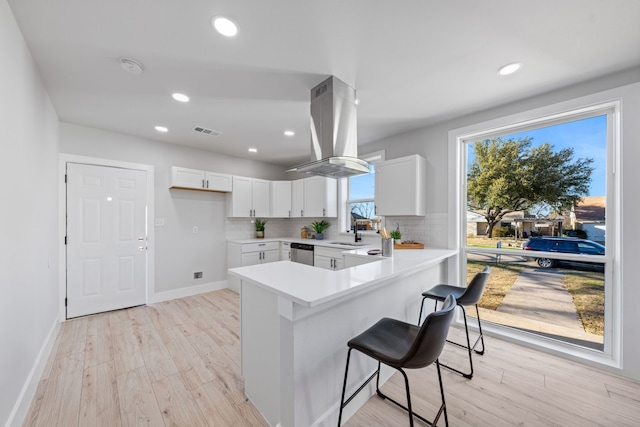 kitchen featuring white cabinetry, light hardwood / wood-style floors, island exhaust hood, backsplash, and sink