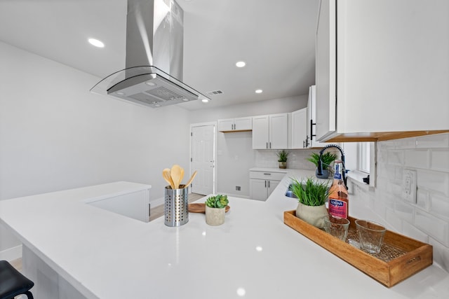 kitchen with kitchen peninsula, island range hood, white cabinetry, and a kitchen bar