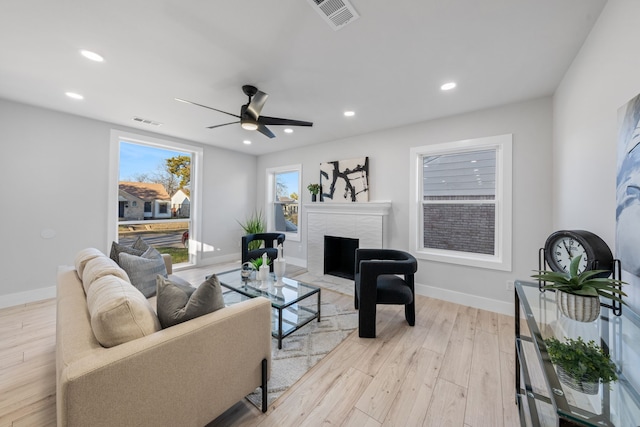 living room with ceiling fan, a high end fireplace, and light hardwood / wood-style flooring