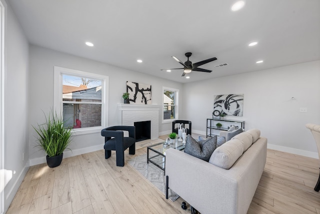 living room featuring light wood-type flooring, ceiling fan, and a fireplace