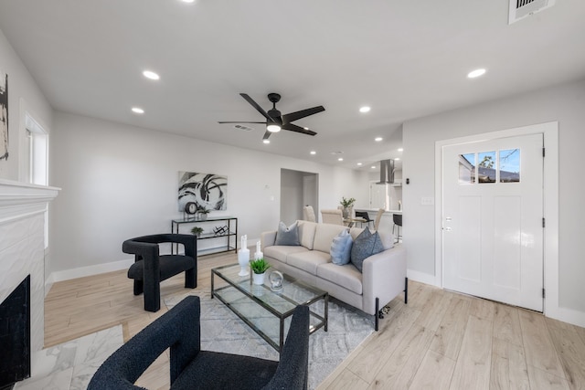 living room with ceiling fan, a fireplace, and light hardwood / wood-style floors